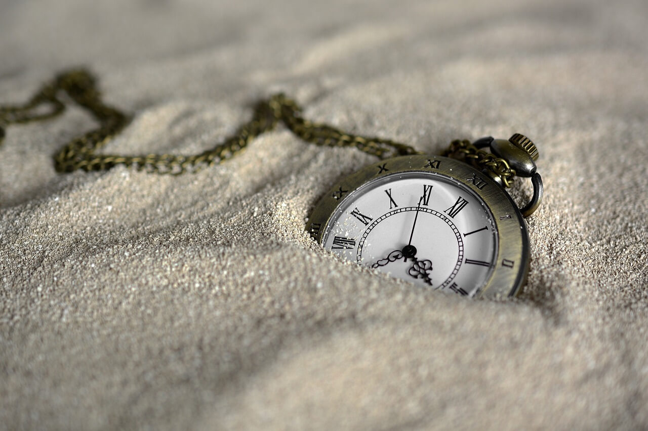 A pocket watch half-buried in fine sand